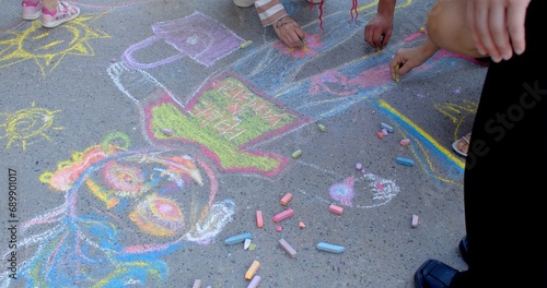 Group of people with children drawing with colorful chalk on the asphalt. Collaboration creativity and self-expression as way for artists with kids to convey their thoughts, feelings, and inspiration.