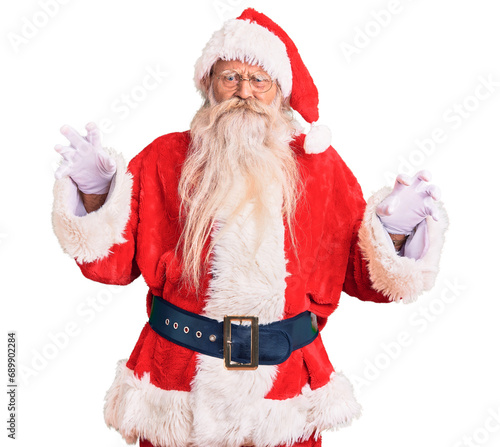 Old senior man with grey hair and long beard wearing traditional santa claus costume smiling funny doing claw gesture as cat, aggressive and sexy expression