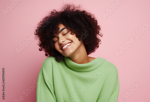 Cheerful young romantic woman expresses self love and care, tilts head and smiles gently, wears green oversized jumper, embraces own body, closes eyes, stands in studio 