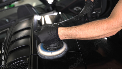 Schwarzer Supersportwagen wird vom Fahrzeugaufbereiter mit der Poliermaschine poliert 