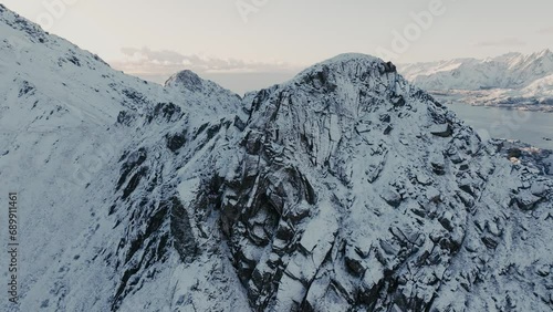 Norway's Lofoten Mount adorned in winter's embrace, with a snow-covered summit against a cold, clear sky. photo