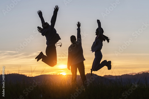 Silhouette three people jumping on mountain sunset sky background.