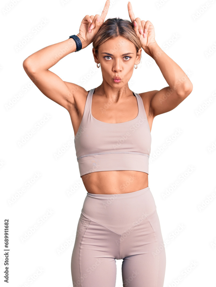 Beautiful caucasian woman wearing sportswear doing funny gesture with finger over head as bull horns Beautiful caucasian woman wearing sportswear doing funny gesture with finger over head as bull horns