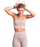 Beautiful caucasian woman wearing sportswear posing funny and crazy with fingers on head as bunny ears, smiling cheerful