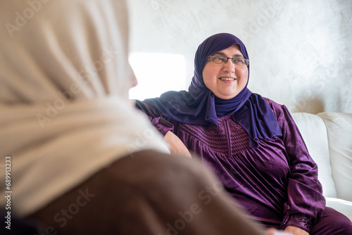 Females talking together wearing hijab in lving room with white background photo