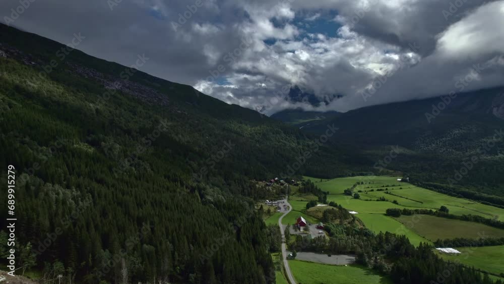 Aerial slider shot over the beautiful green Innerdalen valley in Norway. Meadows and vast forests against the mountains covered with white cumulus clouds. Nordic nature travel concept Aerial slider shot over the beautiful green Innerdalen valley in Norway. Meadows and vast forests against the mountains covered with white cumulus clouds. Nordic nature travel concept