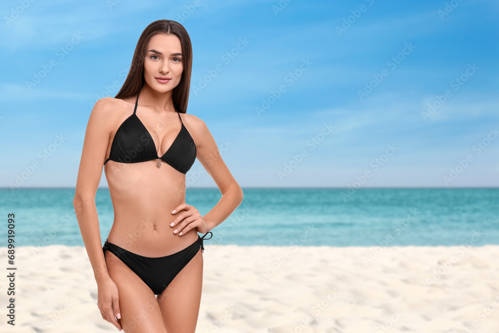 Beautiful woman in stylish black bikini on sandy beach near sea, space for text