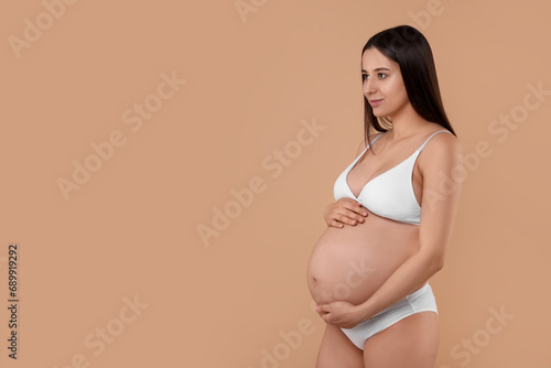 Beautiful pregnant woman in stylish comfortable underwear on beige background, space for text