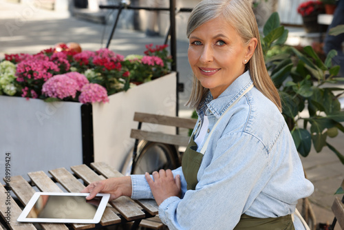 Happy business owner with tablet at table near her flower shop outdoors