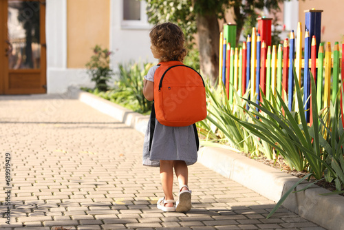 Little girl walking to kindergarten outdoors on sunny day, back view. Space for text photo
