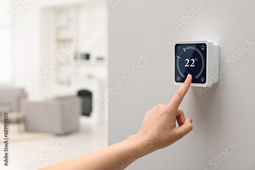 Smart home system. Woman using thermostat indoors, closeup photo