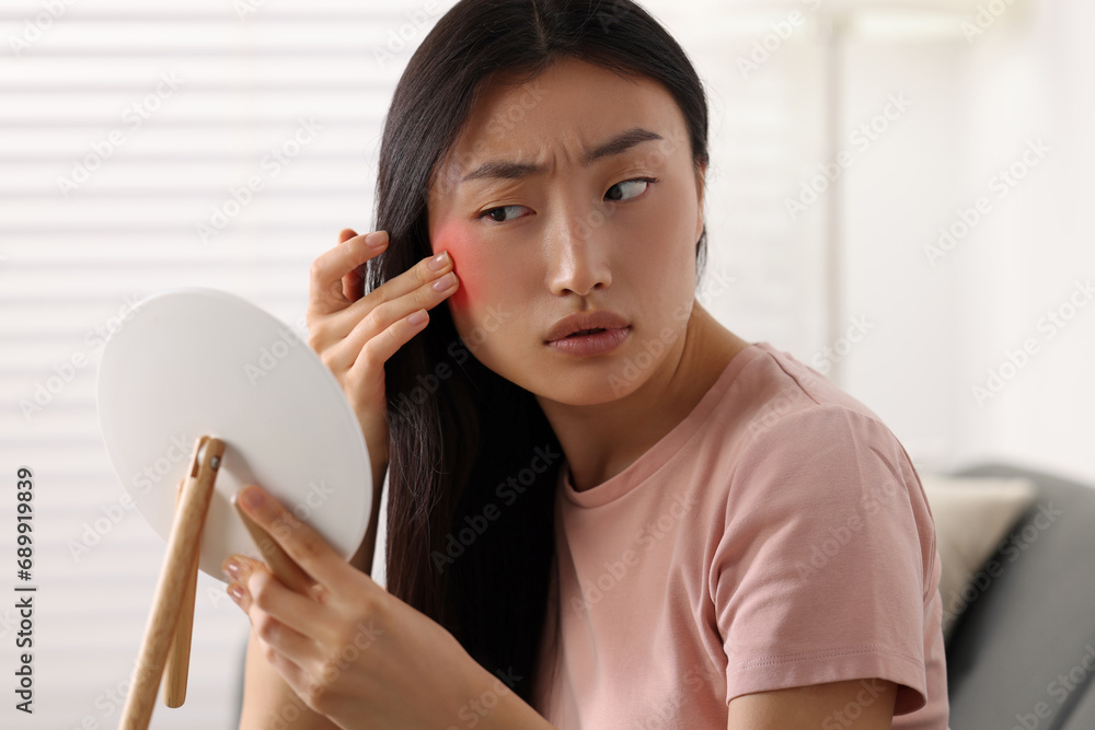 Suffering from allergy. Young woman with mirror checking her face in living room Suffering from allergy. Young woman with mirror checking her face in living room