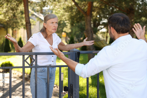 Emotional neighbours having argument near fence outdoors