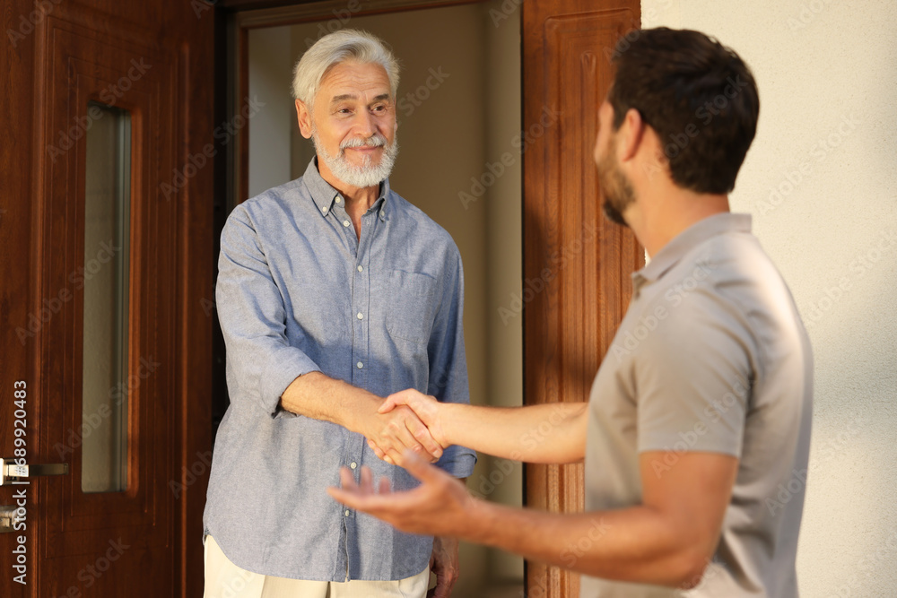Fototapeta premium Friendly relationship with neighbours. Happy men shaking hands near house outdoors