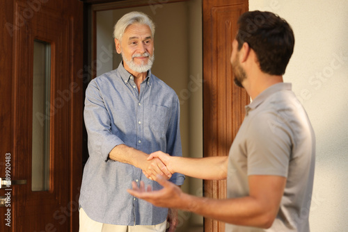 Friendly relationship with neighbours. Happy men shaking hands near house outdoors