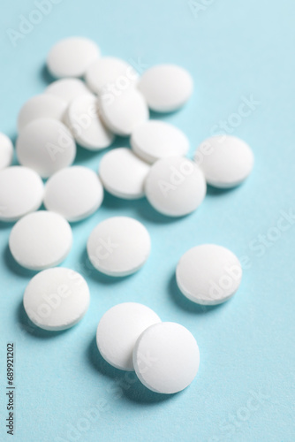 Many white pills on light blue background  closeup