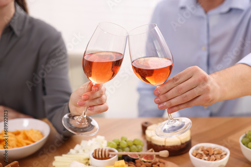 People clinking glasses with rose wine above wooden table indoors  closeup