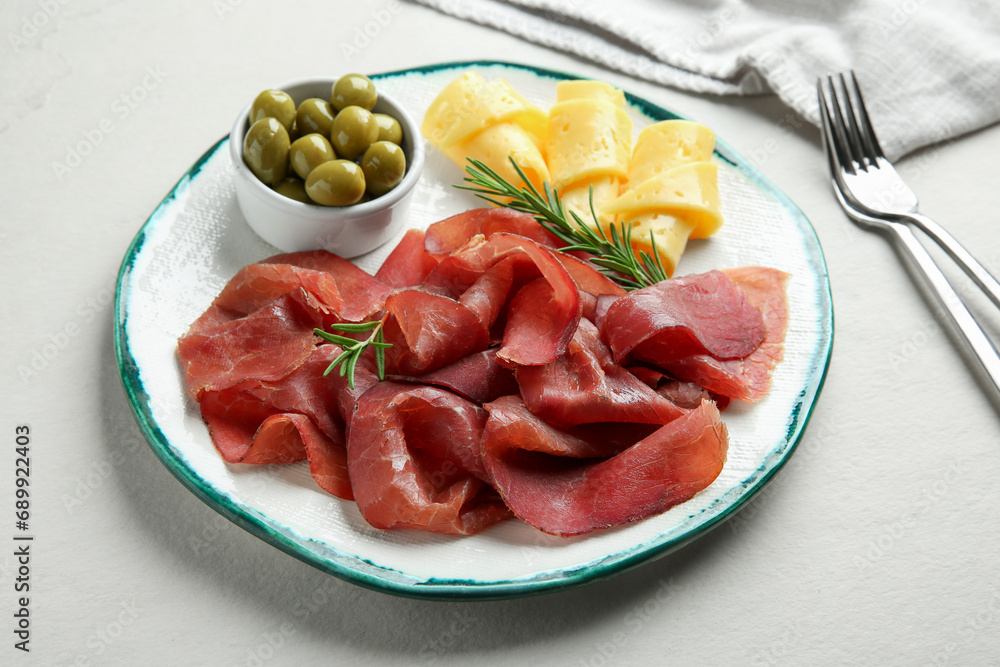 Delicious bresaola, cheese, olives and rosemary on light textured table Delicious bresaola, cheese, olives and rosemary on light textured table