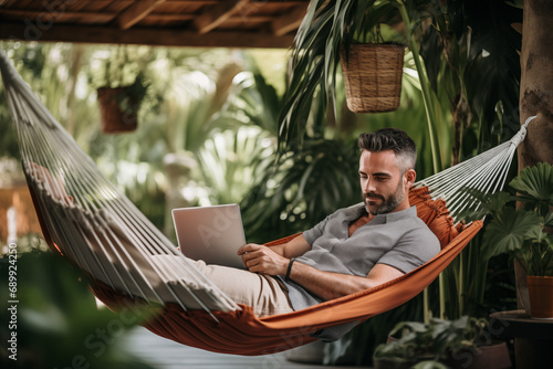 Man working remotely on a laptop while relaxing in a hammock from a tropical destination photo