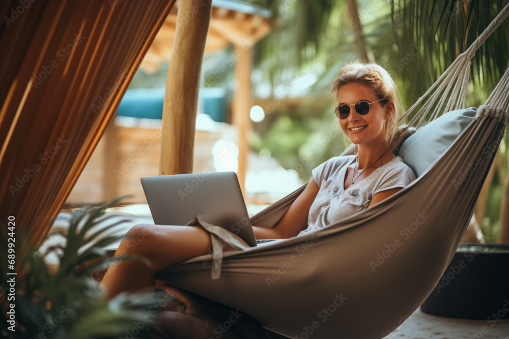 Woman working remotely on a laptop while relaxing in a hammock from a tropical destination