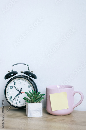 Alarm clock and succulent on the table with sticky notes stick on a cup.