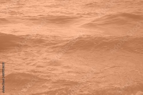 Peach Fuzz toned sea water texture. Pool water with sun reflections. Trendy colour 2024 year.