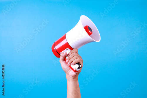 Close up hand holding megaphone over isolated blue background.
