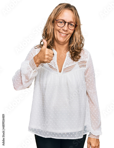 Middle age blonde woman wearing casual white shirt and glasses doing happy thumbs up gesture with hand. approving expression looking at the camera showing success.