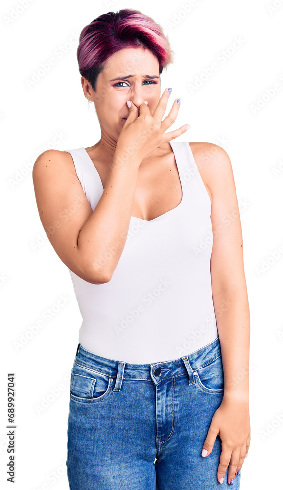 Young beautiful woman with pink hair wearing casual clothes smelling something stinky and disgusting, intolerable smell, holding breath with fingers on nose. bad smell Young beautiful woman with pink hair wearing casual clothes smelling something stinky and disgusting, intolerable smell, holding breath with fingers on nose. bad smell