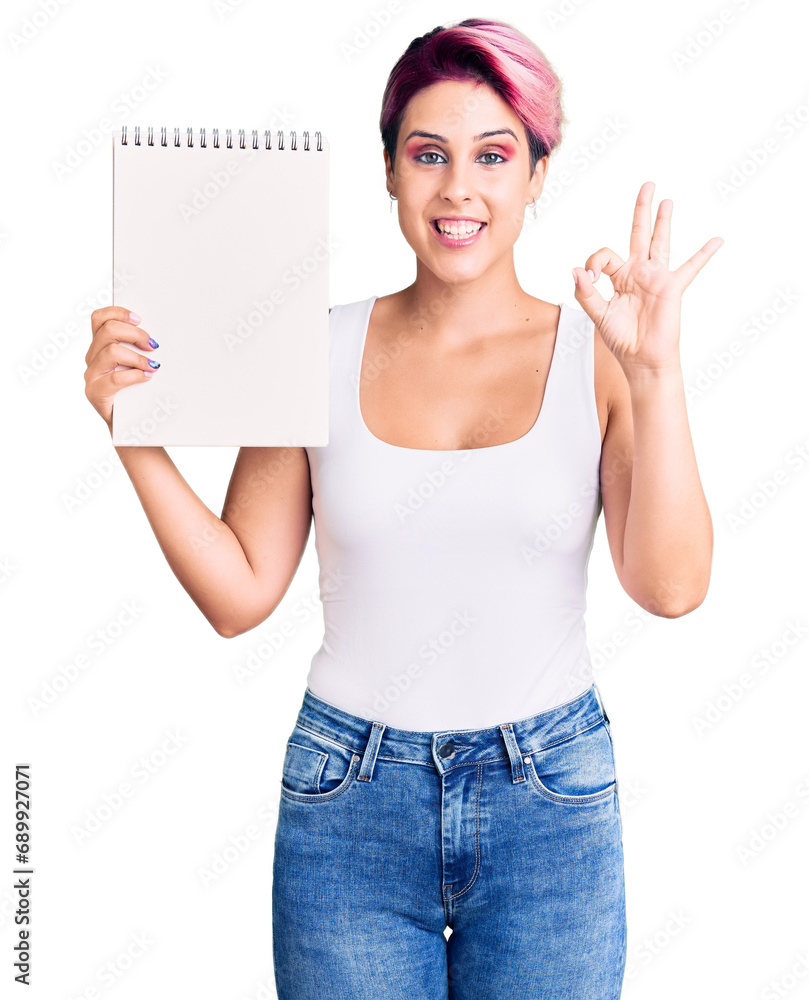 Young beautiful woman with pink hair holding notebook doing ok sign with fingers, smiling friendly gesturing excellent symbol Young beautiful woman with pink hair holding notebook doing ok sign with fingers, smiling friendly gesturing excellent symbol