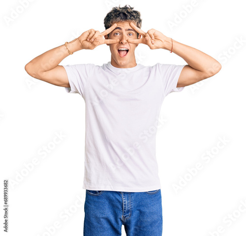 Young handsome man wearing casual white tshirt doing peace symbol with fingers over face, smiling cheerful showing victory