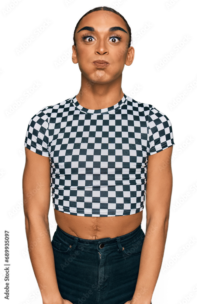 Hispanic transgender man wearing make up and long hair wearing modern clothes puffing cheeks with funny face. mouth inflated with air, crazy expression. Hispanic transgender man wearing make up and long hair wearing modern clothes puffing cheeks with funny face. mouth inflated with air, crazy expression.
