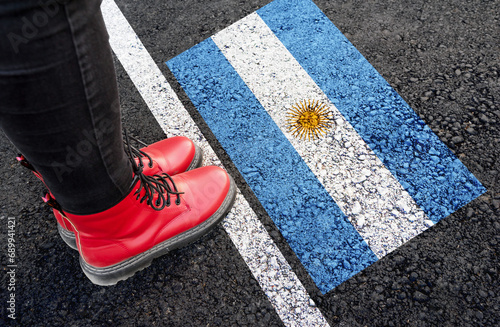 a womman with a boots standing on asphalt next to flag of Argentina and border
 photo