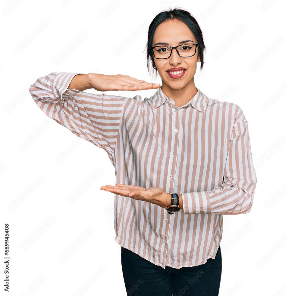 Fototapeta premium Young hispanic girl wearing casual clothes and glasses gesturing with hands showing big and large size sign, measure symbol. smiling looking at the camera. measuring concept.