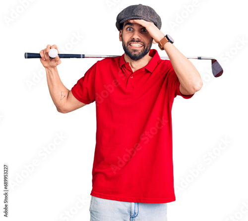 Young handsome man with beard playing golf holding club and ball stressed and frustrated with hand on head, surprised and angry face