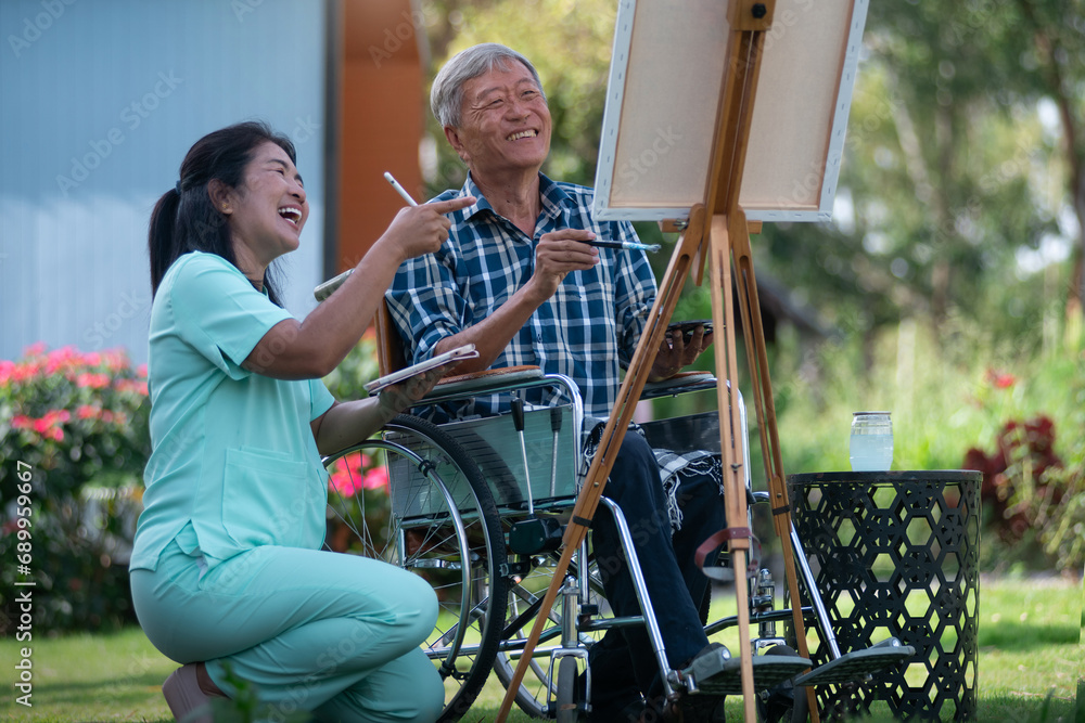 Senior man in wheelchair relaxes his mind by painting on a canvas frame with his caregiver nearby encouraging him, concept of caring for the elderly to be happy