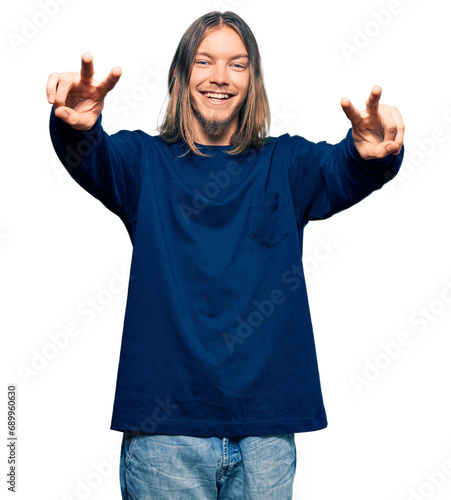 Handsome caucasian man with long hair wearing casual winter sweater smiling with tongue out showing fingers of both hands doing victory sign. number two.