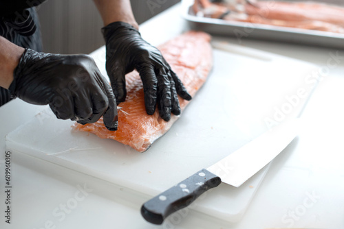 Close up, Japanese chef's hands uses tweezers to remove fish bones from fresh salmon on a cutting board, steps for preparing ingredients for Japanese cooking