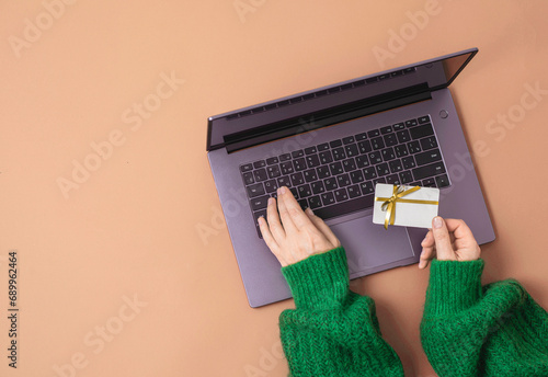 Christmas shopping concept. Flat lie. Women's hands in a green sweater on laptop keyboard with Gift card on a red background