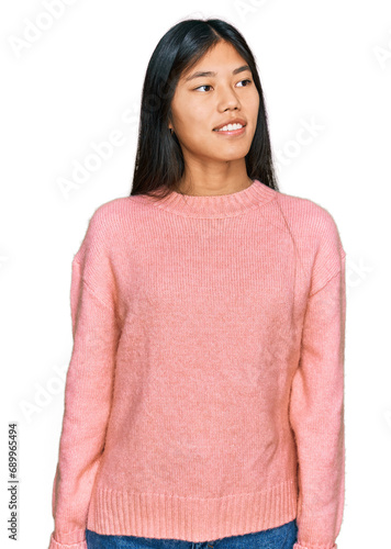 Beautiful young asian woman wearing casual winter sweater looking away to side with smile on face, natural expression. laughing confident.