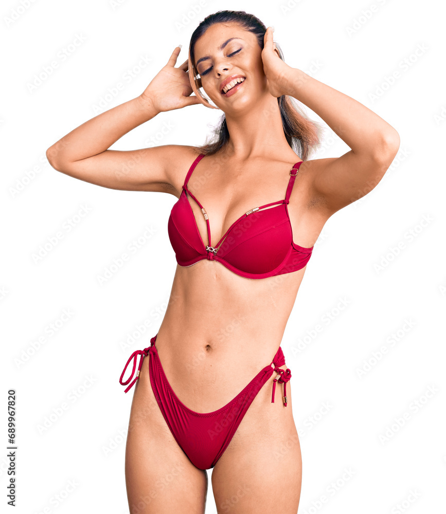 Young beautiful woman wearing bikini relaxing and stretching, arms and hands behind head and neck smiling happy Young beautiful woman wearing bikini relaxing and stretching, arms and hands behind head and neck smiling happy
