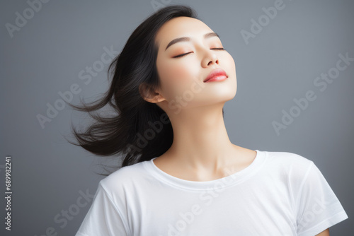 Beautiful young Asian woman wearing a white t-shirt Close your eyes and feel happy and relaxed. Isolated empty space on a gray background. photo