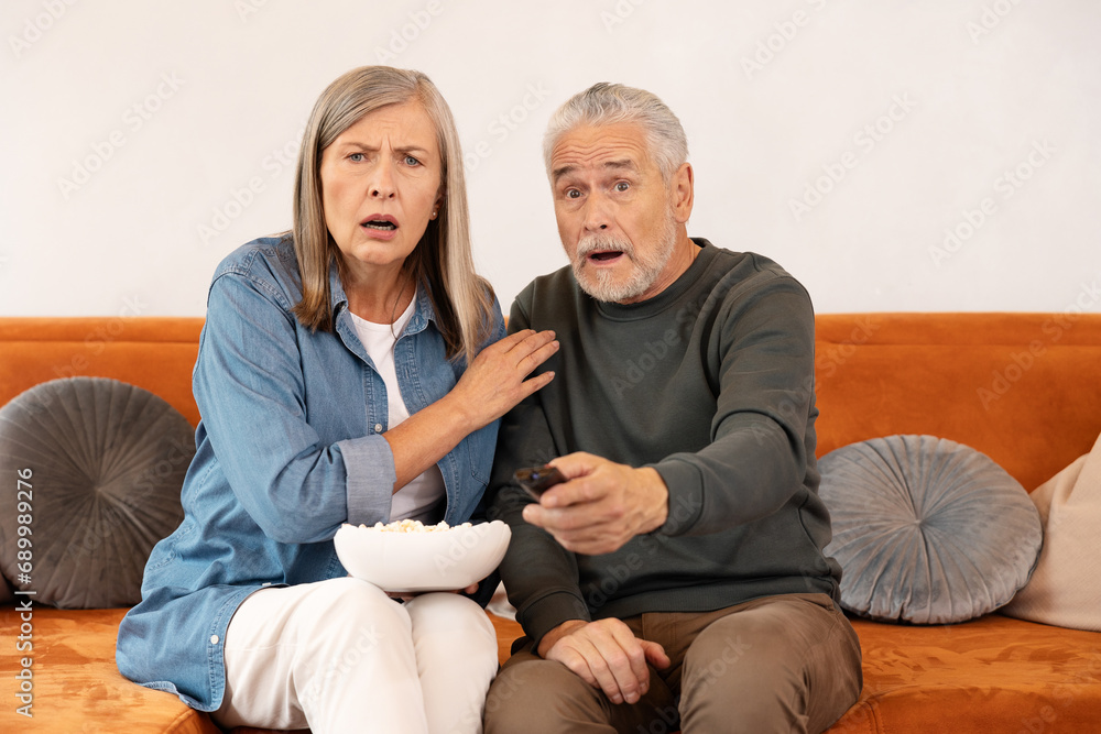 Couple elderly watching horror movie at home eating popcorn and making scary facial .expressions. Couple elderly watching horror movie at home eating popcorn and making scary facial .expressions.