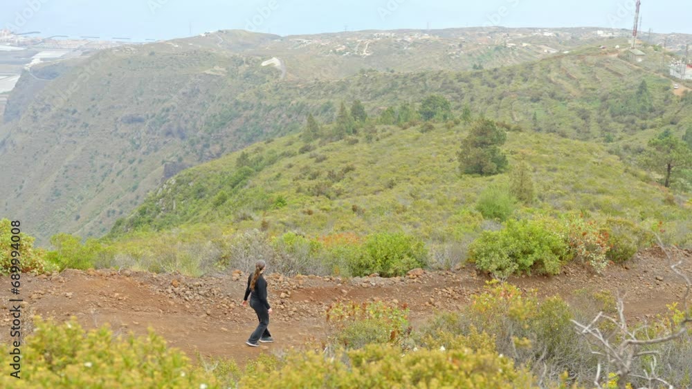 Girl walking down dirt path, view over coast and green hills of Tenerife Girl walking down dirt path, view over coast and green hills of Tenerife