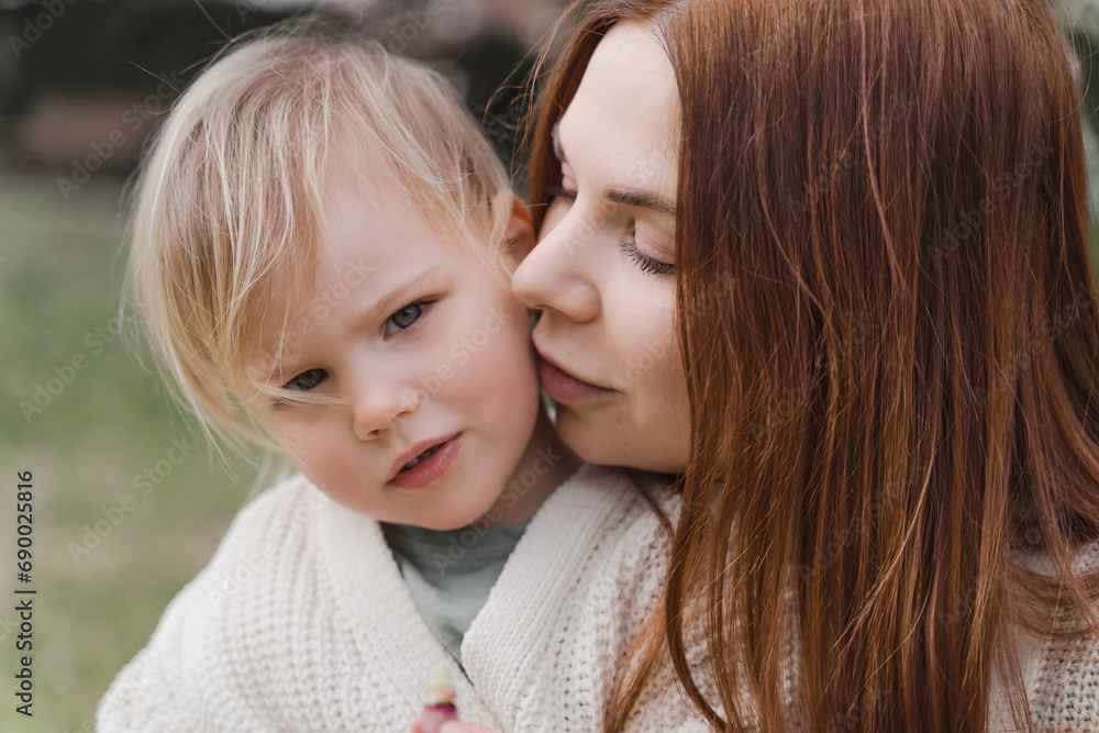 A woman kiss her little daughter near a blooming magnolia tree. A woman kiss her little daughter near a blooming magnolia tree.