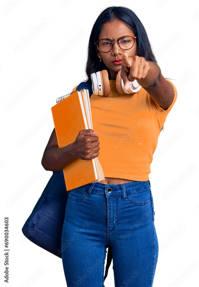 Young indian girl holding student backpack and books pointing with finger to the camera and to you, confident gesture looking serious Young indian girl holding student backpack and books pointing with finger to the camera and to you, confident gesture looking serious