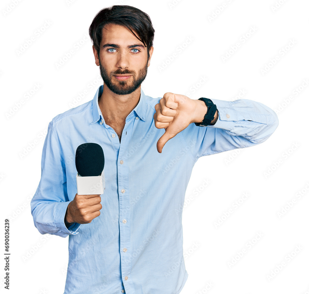 Hispanic man with blue eyes holding reporter microphone with angry face, negative sign showing dislike with thumbs down, rejection concept Hispanic man with blue eyes holding reporter microphone with angry face, negative sign showing dislike with thumbs down, rejection concept