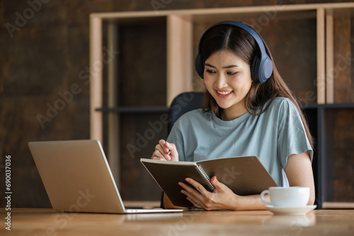 Young female student wearing headphones sits intently and happily studying online on her laptop in the living room at home.