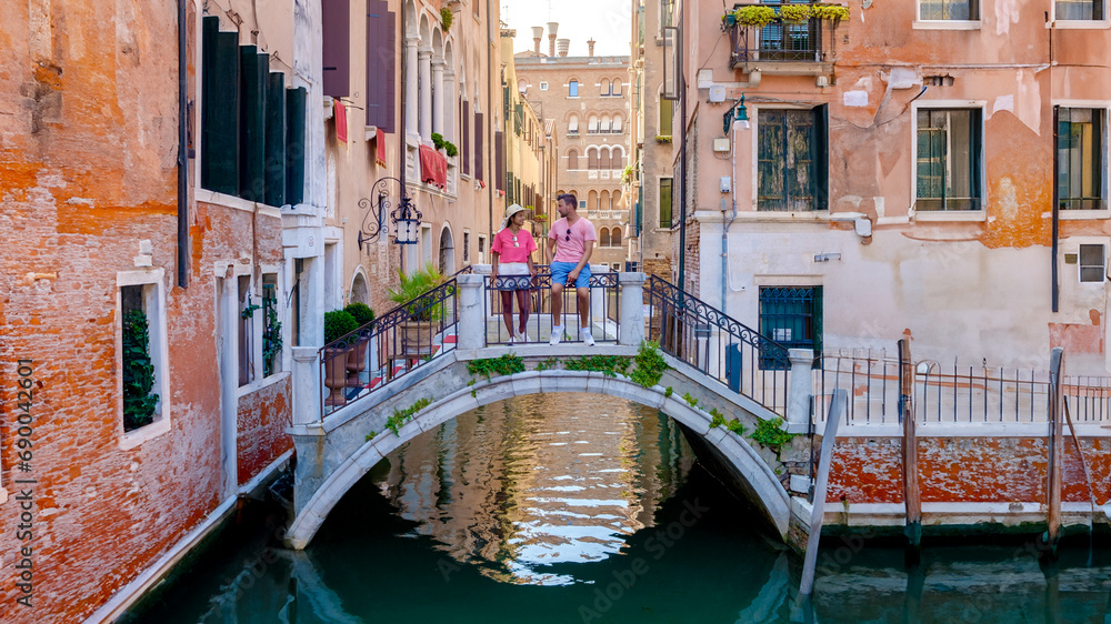 a couple of men and women on a city trip in Venice Italy sitting above a bridge at the canals of Venice, during a city trip in summer in Europe