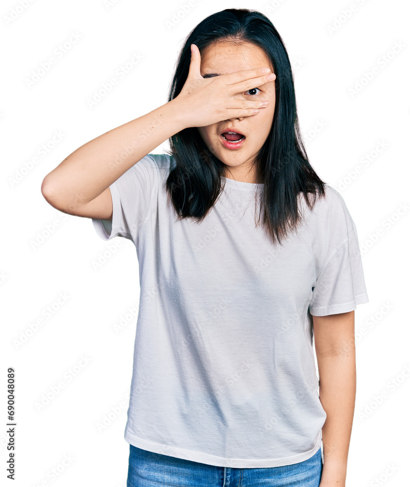 Young chinese woman wearing casual white t shirt peeking in shock covering face and eyes with hand, looking through fingers with embarrassed expression. Young chinese woman wearing casual white t shirt peeking in shock covering face and eyes with hand, looking through fingers with embarrassed expression.